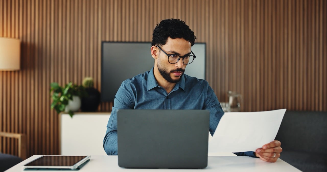 AP specialist comparing a paper invoice against vendor master data on his laptop